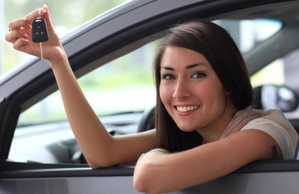 Smiling young woman leaning out car window holding car keys