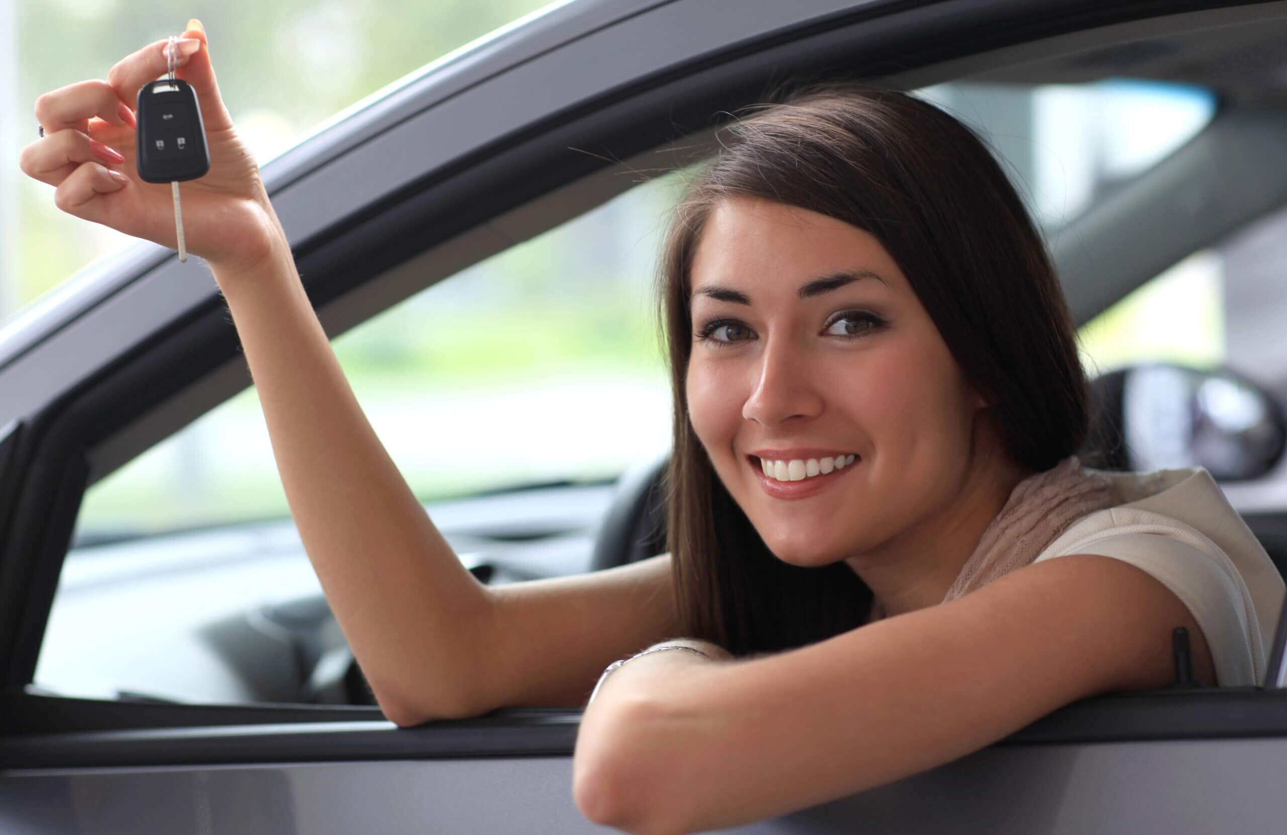 Smiling young woman leaning out car window holding car keys