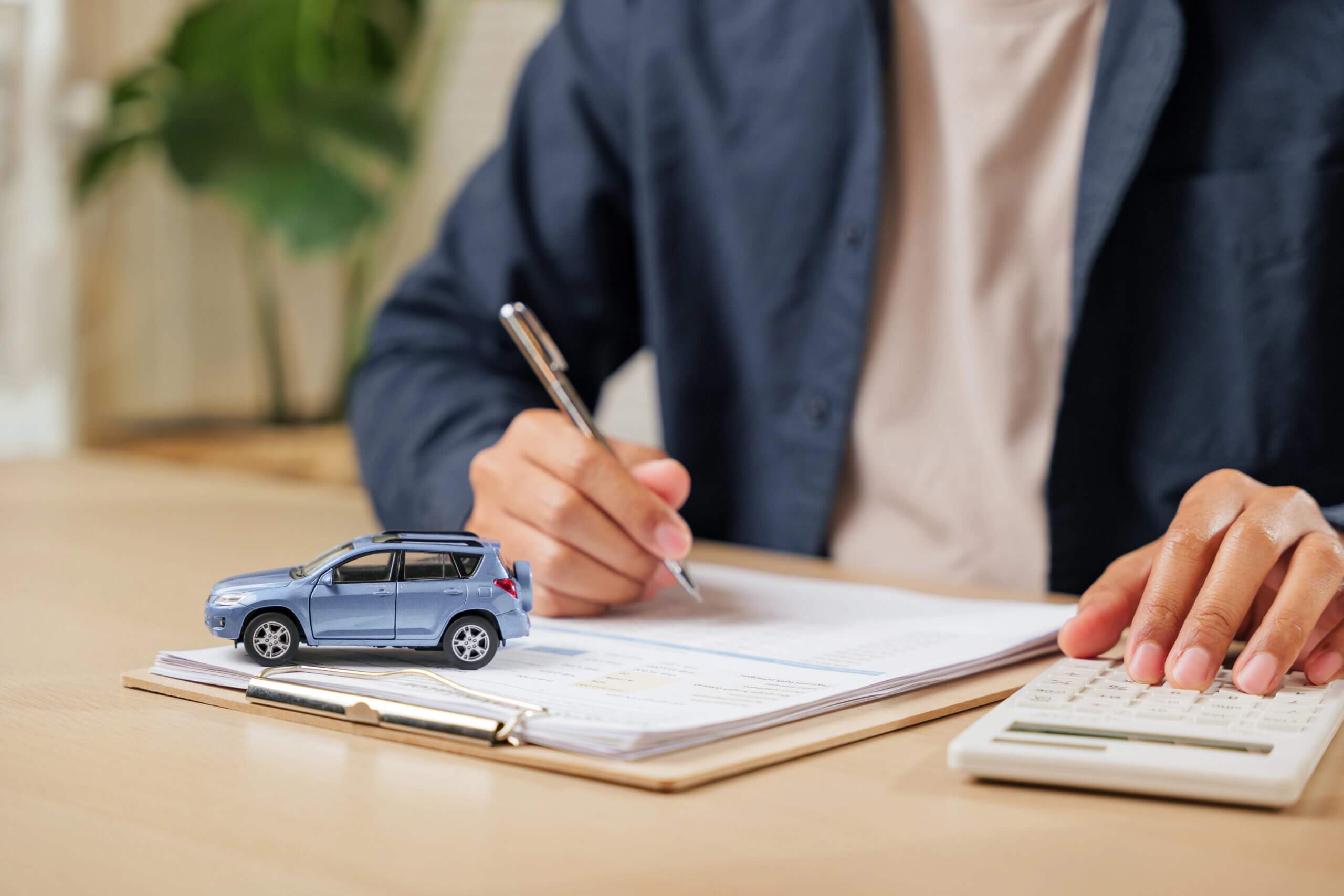 Close-up of man filling out form, tiny toy car on desk