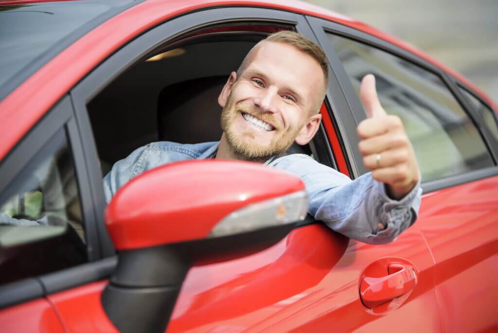 Smiling man giving thumbs up out of car window